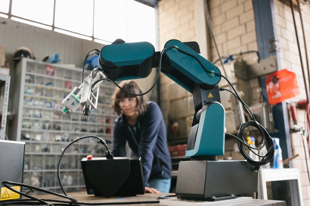 Brazo robótico articulado en un laboratorio de prototipado, con una ingeniera observando: innovación y adopción en la operación